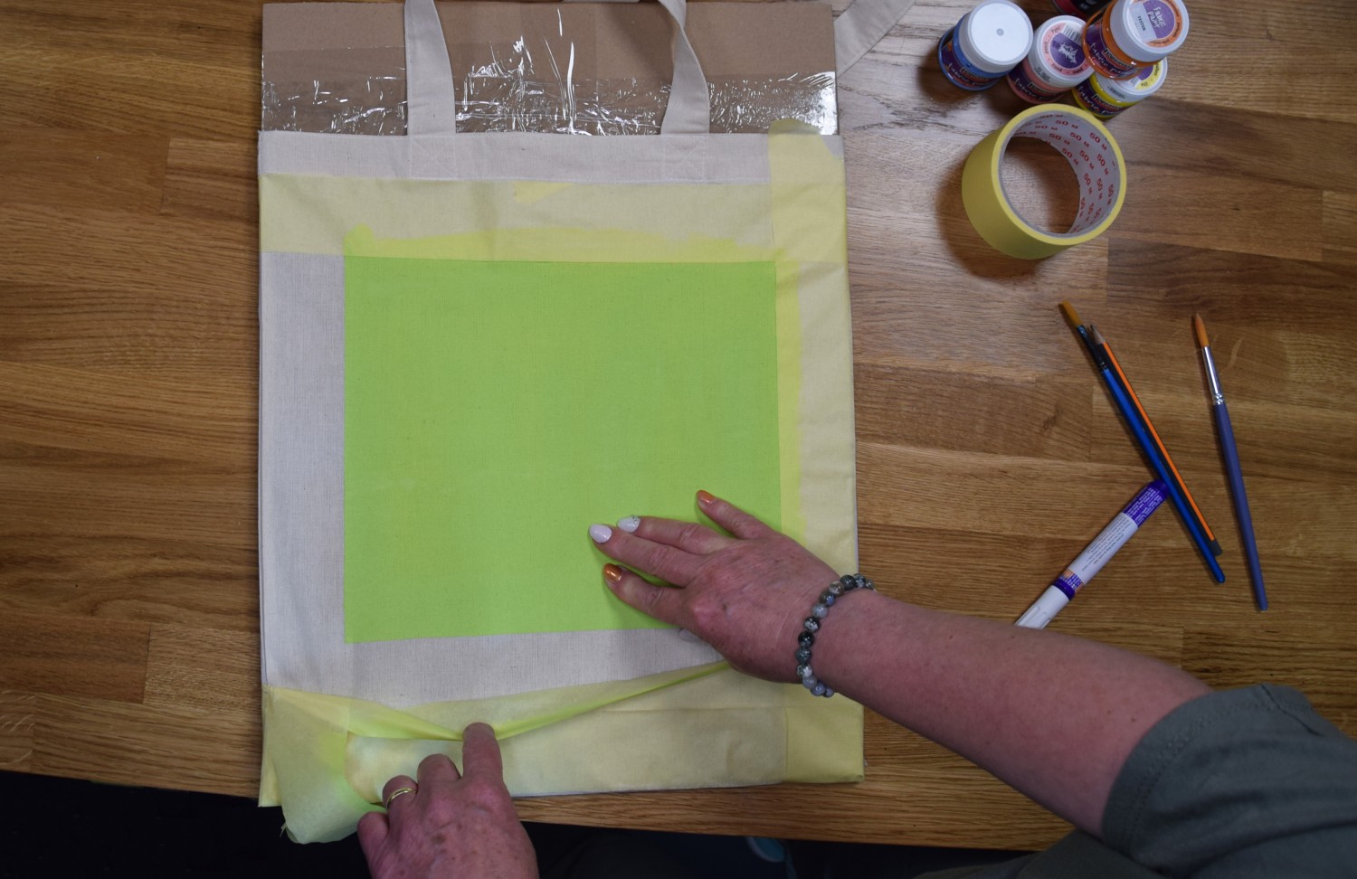 Žena odlepuje lepiacu pásku po zaschnutí zelenej farby.